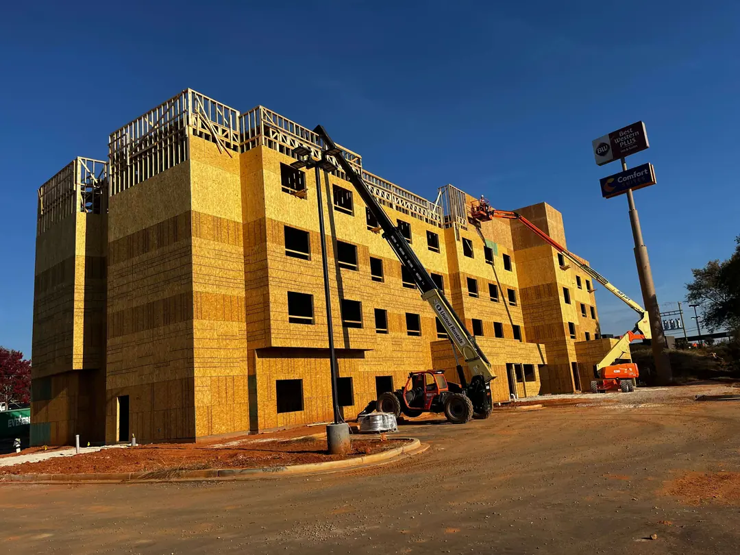 Four-story hotel under construction in bare wood sheathing, with two lifts and a worker in a basket near the top